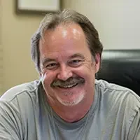 Portrait of Jim A., an older balding man, smiling with relief as he signs closing documents